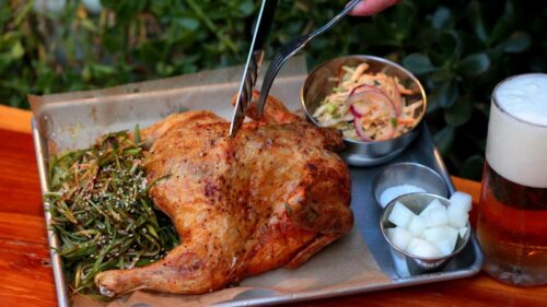 A delicious roasted chicken served with sides and a refreshing beer, captured outdoors.