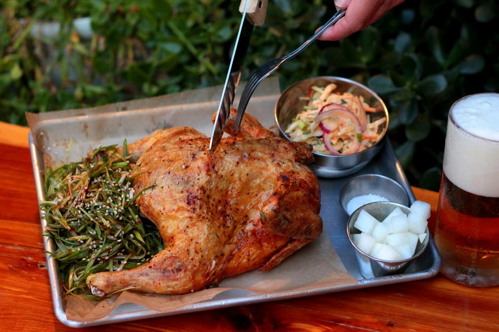 A delicious roasted chicken served with sides and a refreshing beer, captured outdoors.